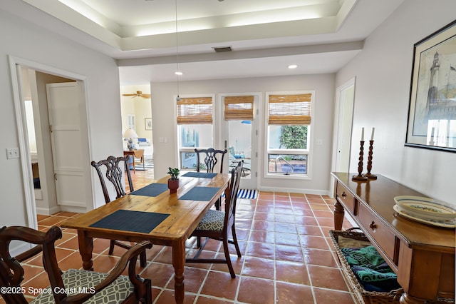 tiled dining space with ceiling fan and a raised ceiling