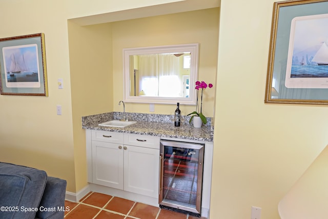 bar with light tile patterned flooring, sink, white cabinets, beverage cooler, and light stone counters