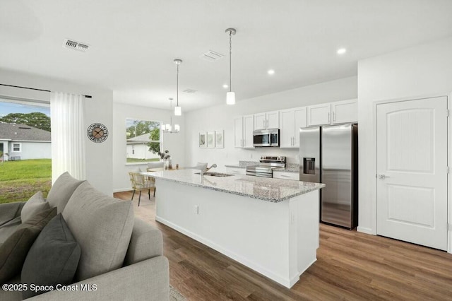 kitchen featuring a kitchen island with sink, hanging light fixtures, stainless steel appliances, light stone countertops, and white cabinets