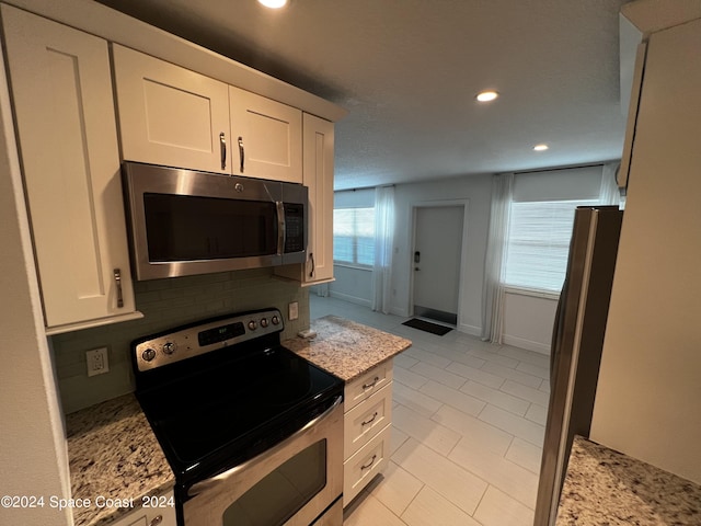 kitchen featuring light stone counters, tasteful backsplash, white cabinets, and appliances with stainless steel finishes