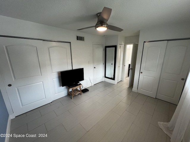 unfurnished bedroom featuring multiple closets, a textured ceiling, and ceiling fan