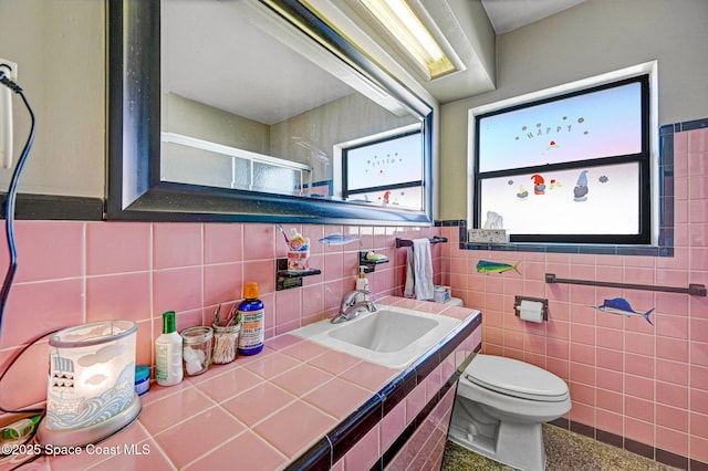 bathroom with toilet, sink, and tile walls