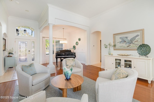 living room featuring ornamental molding, a towering ceiling, light hardwood / wood-style flooring, and decorative columns