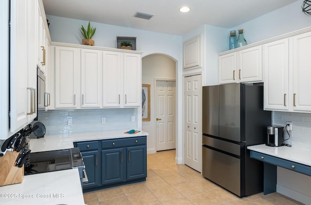 kitchen with stainless steel refrigerator, white cabinetry, backsplash, light tile patterned floors, and blue cabinetry