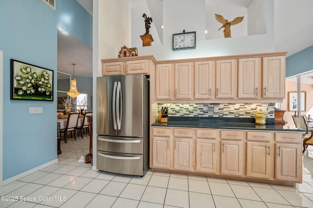 kitchen with a towering ceiling, stainless steel fridge, and light brown cabinetry