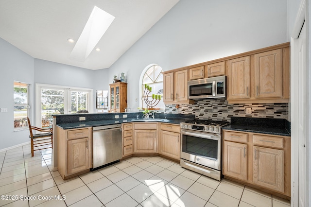 kitchen with light tile patterned flooring, a skylight, backsplash, kitchen peninsula, and stainless steel appliances