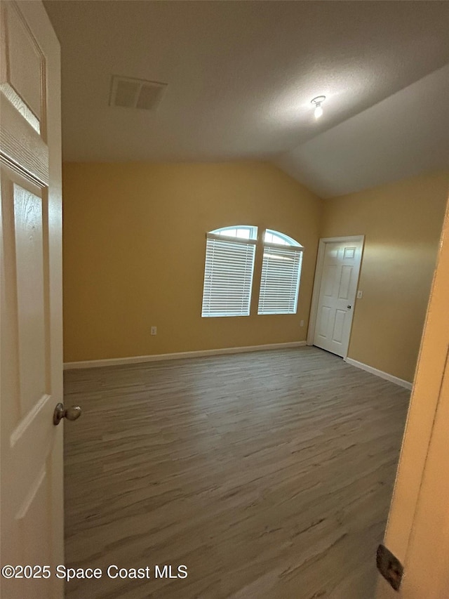 spare room with hardwood / wood-style flooring and vaulted ceiling