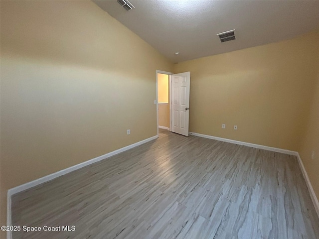 spare room featuring vaulted ceiling and light hardwood / wood-style floors