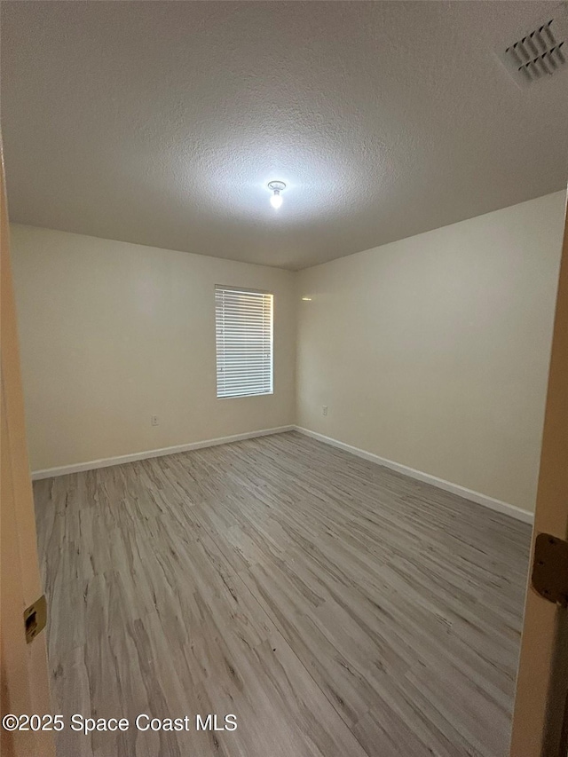 empty room with a textured ceiling and light hardwood / wood-style flooring