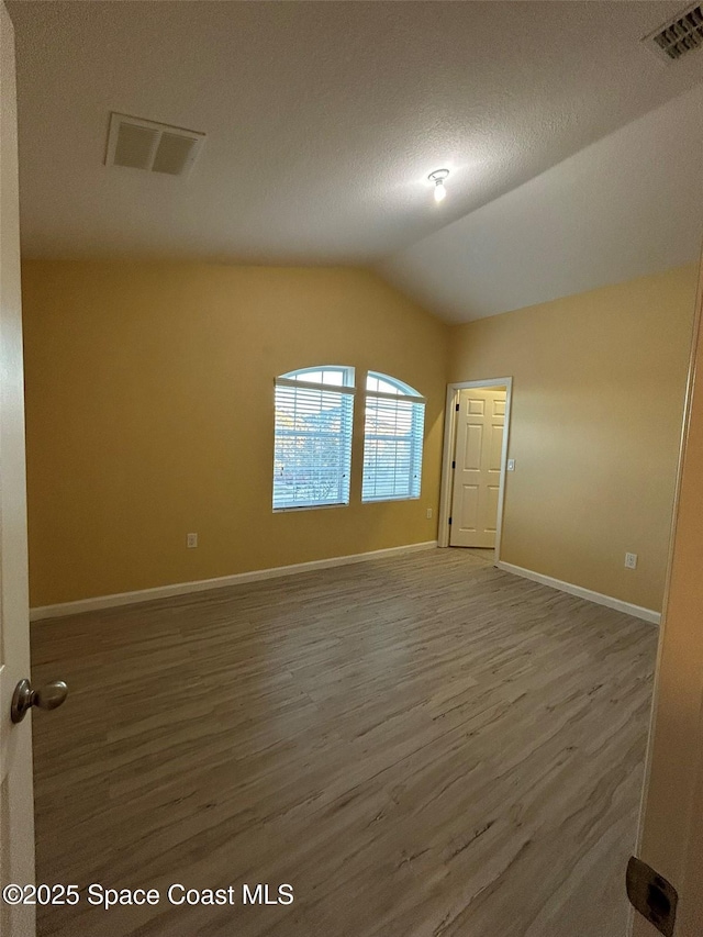 empty room featuring wood-type flooring, lofted ceiling, and a textured ceiling