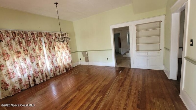 unfurnished dining area with built in shelves, an inviting chandelier, and dark wood-type flooring