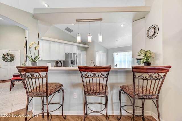 kitchen with lofted ceiling, a breakfast bar area, hanging light fixtures, stainless steel refrigerator with ice dispenser, and white cabinets