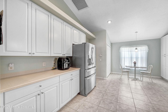 kitchen featuring light tile patterned floors, decorative light fixtures, stainless steel fridge, and white cabinets