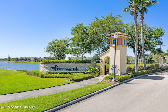 community / neighborhood sign featuring a water view and a yard