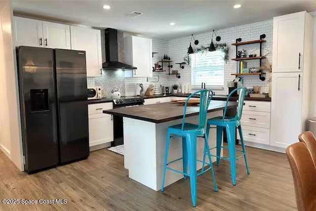 kitchen featuring white cabinetry, wall chimney range hood, electric range, and stainless steel refrigerator with ice dispenser