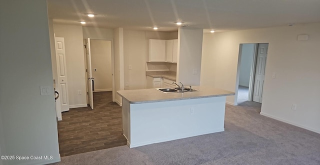 kitchen featuring carpet flooring, sink, an island with sink, and white cabinets