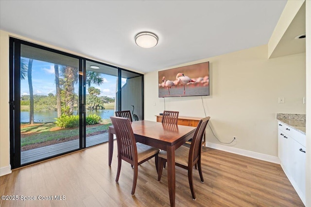 dining space with light hardwood / wood-style flooring, a wall of windows, and a water view