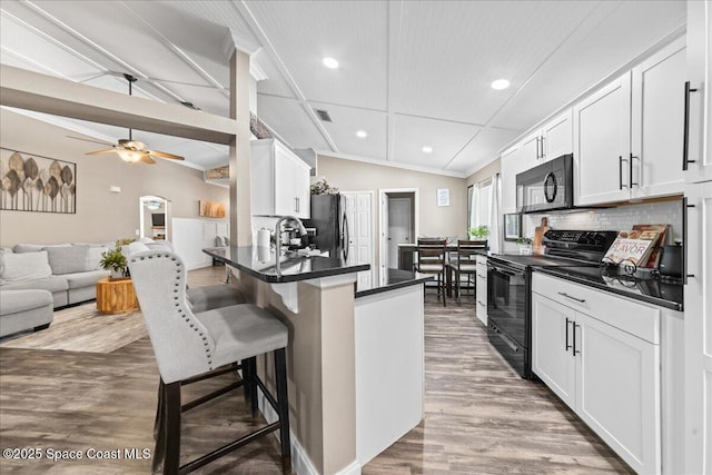 kitchen featuring white cabinetry, lofted ceiling, a breakfast bar, and black appliances