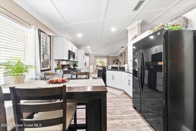 kitchen featuring white cabinetry, dishwashing machine, stove, light hardwood / wood-style floors, and black fridge