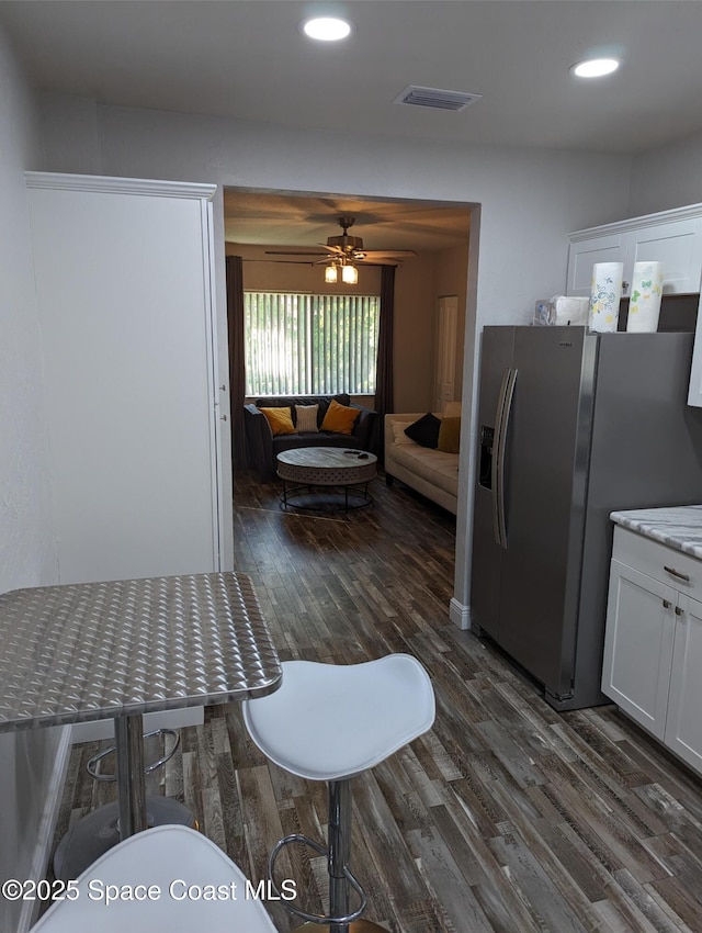 kitchen with stainless steel refrigerator with ice dispenser, dark wood-type flooring, ceiling fan, light stone countertops, and white cabinets