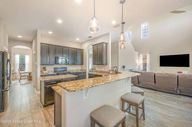 kitchen with a kitchen bar, hanging light fixtures, kitchen peninsula, light stone countertops, and stove