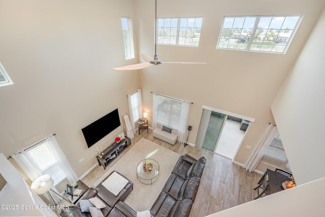 living room with ceiling fan, a towering ceiling, and light hardwood / wood-style flooring