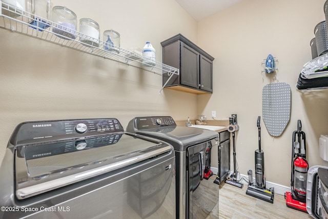 clothes washing area with cabinets, sink, light hardwood / wood-style flooring, and washing machine and clothes dryer