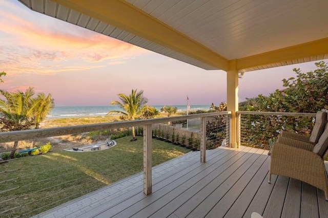 deck at dusk with a view of the beach, a water view, and a lawn