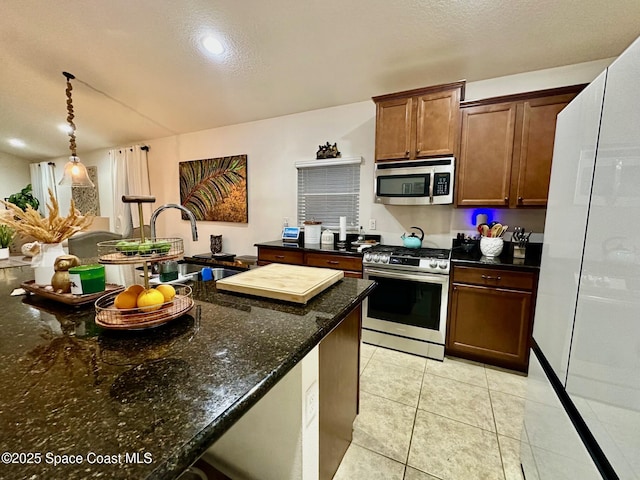 kitchen with pendant lighting, sink, light tile patterned floors, appliances with stainless steel finishes, and dark stone counters