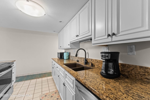 kitchen with appliances with stainless steel finishes, white cabinetry, sink, dark stone counters, and light tile patterned floors