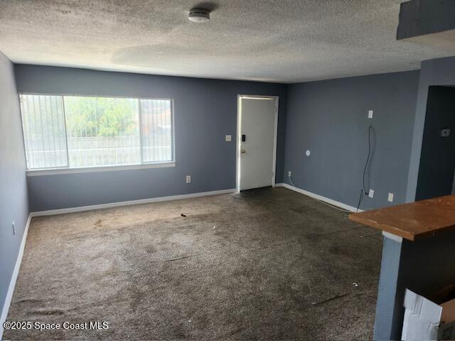 unfurnished living room featuring dark colored carpet and a textured ceiling