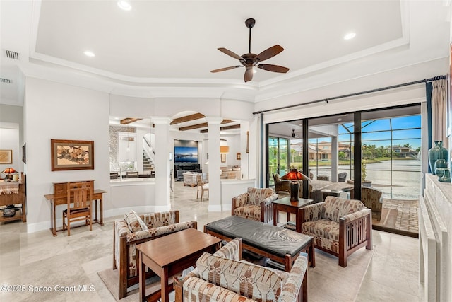 living room with ceiling fan, a tray ceiling, and ornate columns