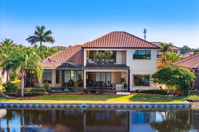 back of property featuring a lawn, glass enclosure, a water view, a patio area, and a balcony