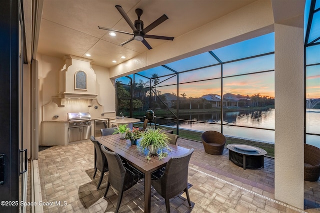 patio terrace at dusk featuring a lanai, an outdoor fire pit, a water view, area for grilling, and grilling area