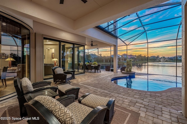 pool at dusk with a water view, glass enclosure, ceiling fan, and a patio area