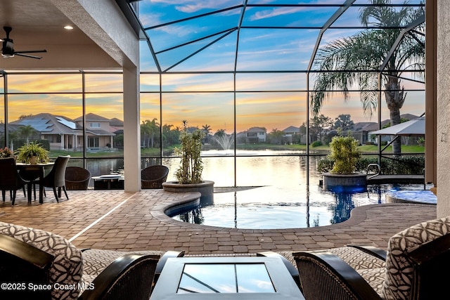 pool at dusk featuring a water view, a lanai, and a patio