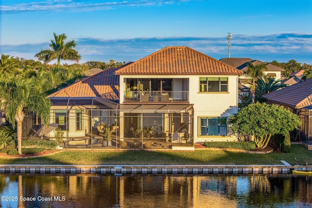 rear view of property featuring a patio area, a water view, a balcony, glass enclosure, and a lawn