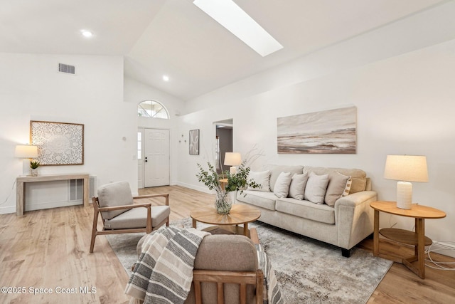 living room featuring a skylight, high vaulted ceiling, and light wood-type flooring