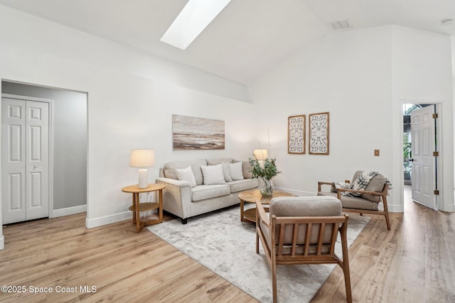 living room featuring high vaulted ceiling, light hardwood / wood-style floors, and a skylight