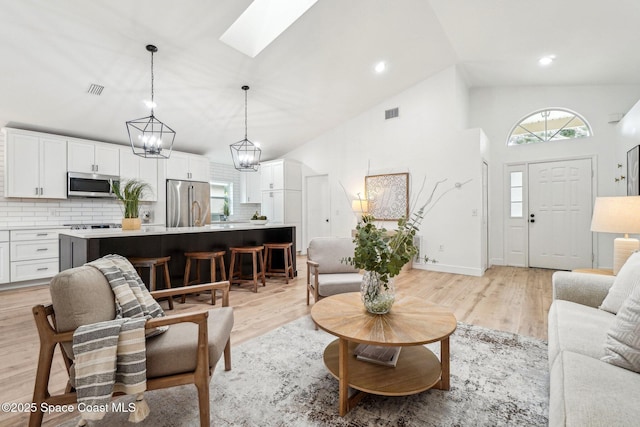 living room featuring sink, a chandelier, a skylight, high vaulted ceiling, and light hardwood / wood-style flooring