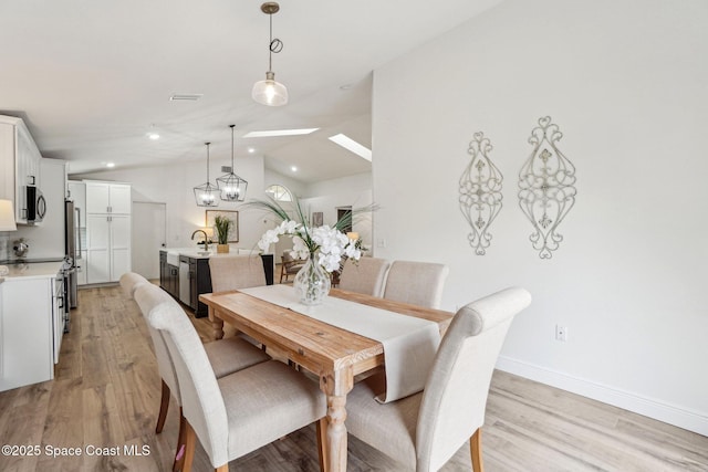 dining area with sink, lofted ceiling with skylight, light hardwood / wood-style floors, and a chandelier