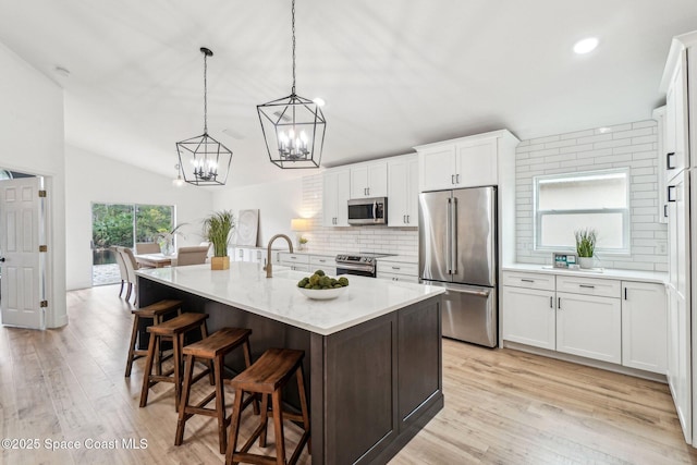 kitchen featuring sink, decorative light fixtures, appliances with stainless steel finishes, an island with sink, and white cabinets