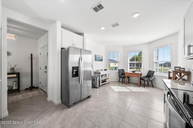 kitchen with light tile patterned floors, a textured ceiling, stainless steel appliances, and white cabinets