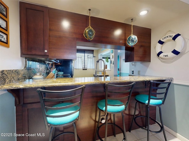 kitchen featuring light tile patterned floors, light stone counters, a kitchen bar, decorative backsplash, and kitchen peninsula