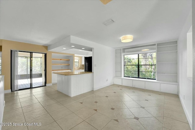 kitchen with light tile patterned flooring, a healthy amount of sunlight, kitchen peninsula, and built in features