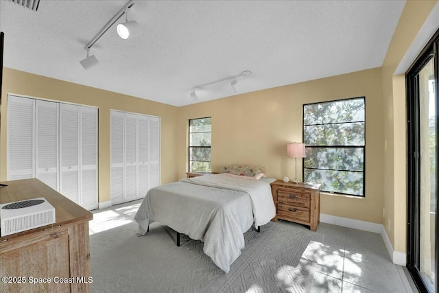 bedroom with multiple windows, multiple closets, rail lighting, and a textured ceiling