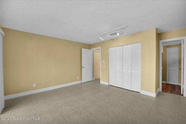 unfurnished bedroom with light tile patterned floors, track lighting, a closet, and a textured ceiling