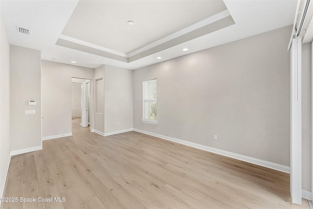 empty room with a raised ceiling and light hardwood / wood-style floors