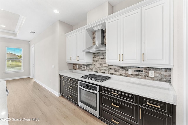 kitchen with wall chimney range hood, appliances with stainless steel finishes, light hardwood / wood-style floors, white cabinets, and decorative backsplash