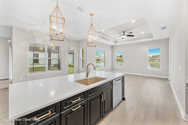 kitchen featuring sink, light stone counters, hanging light fixtures, a tray ceiling, and dishwasher